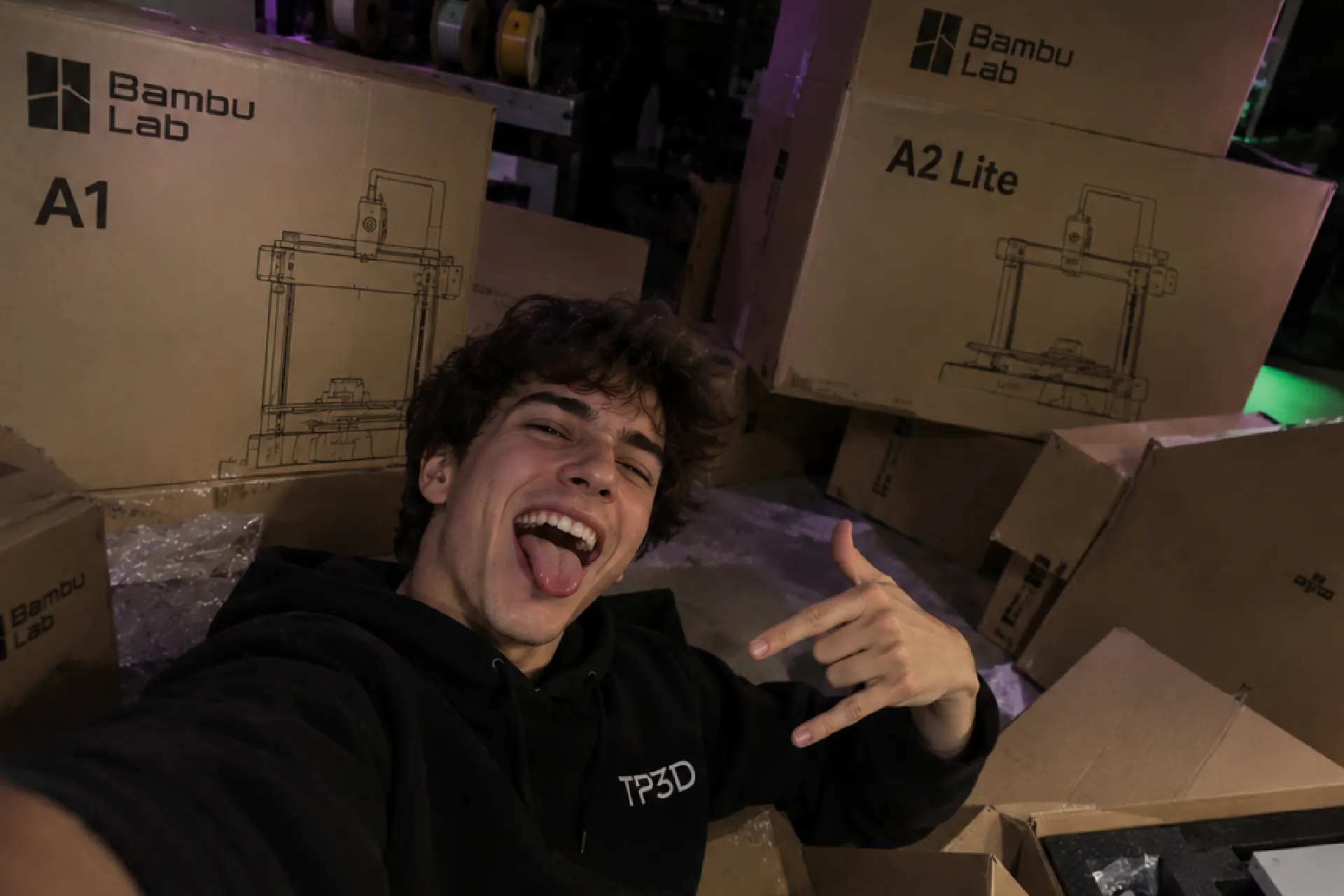 Chico de TP3D celebrando entre cajas de impresoras Bambu Lab A1 y A2 Lite